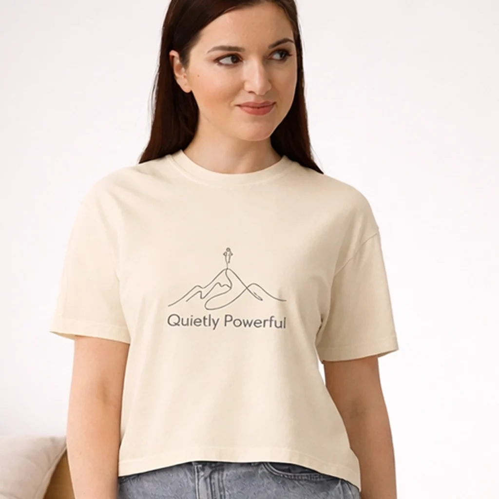 A brunette Gen Z lady wearing Nourivra Co. original colored graphic design of Quietly Powerful cream boxy tee shirt